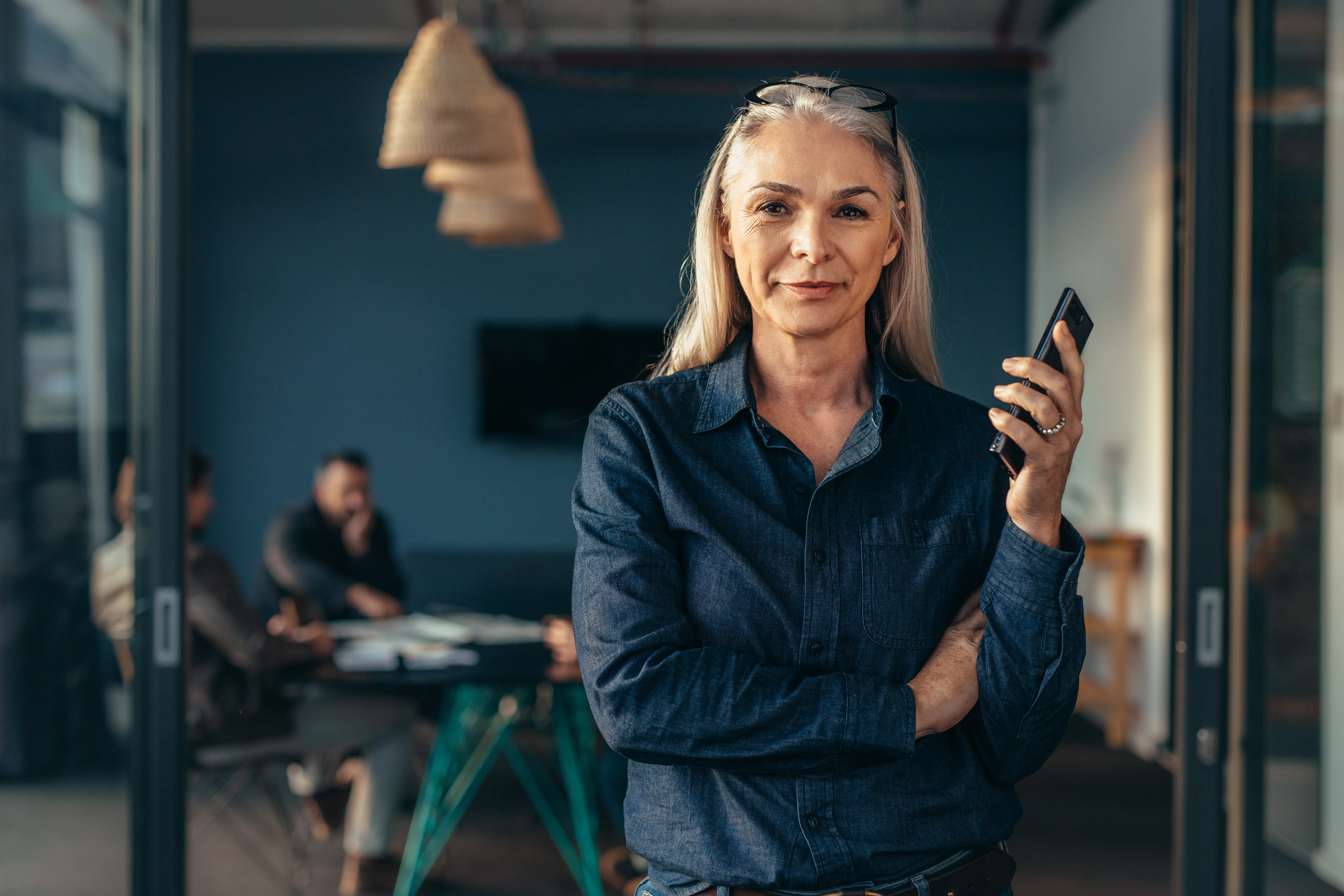 Ältere Geschäftsfrau mit Smartphone in der Hand in einem modernen Meetingraum