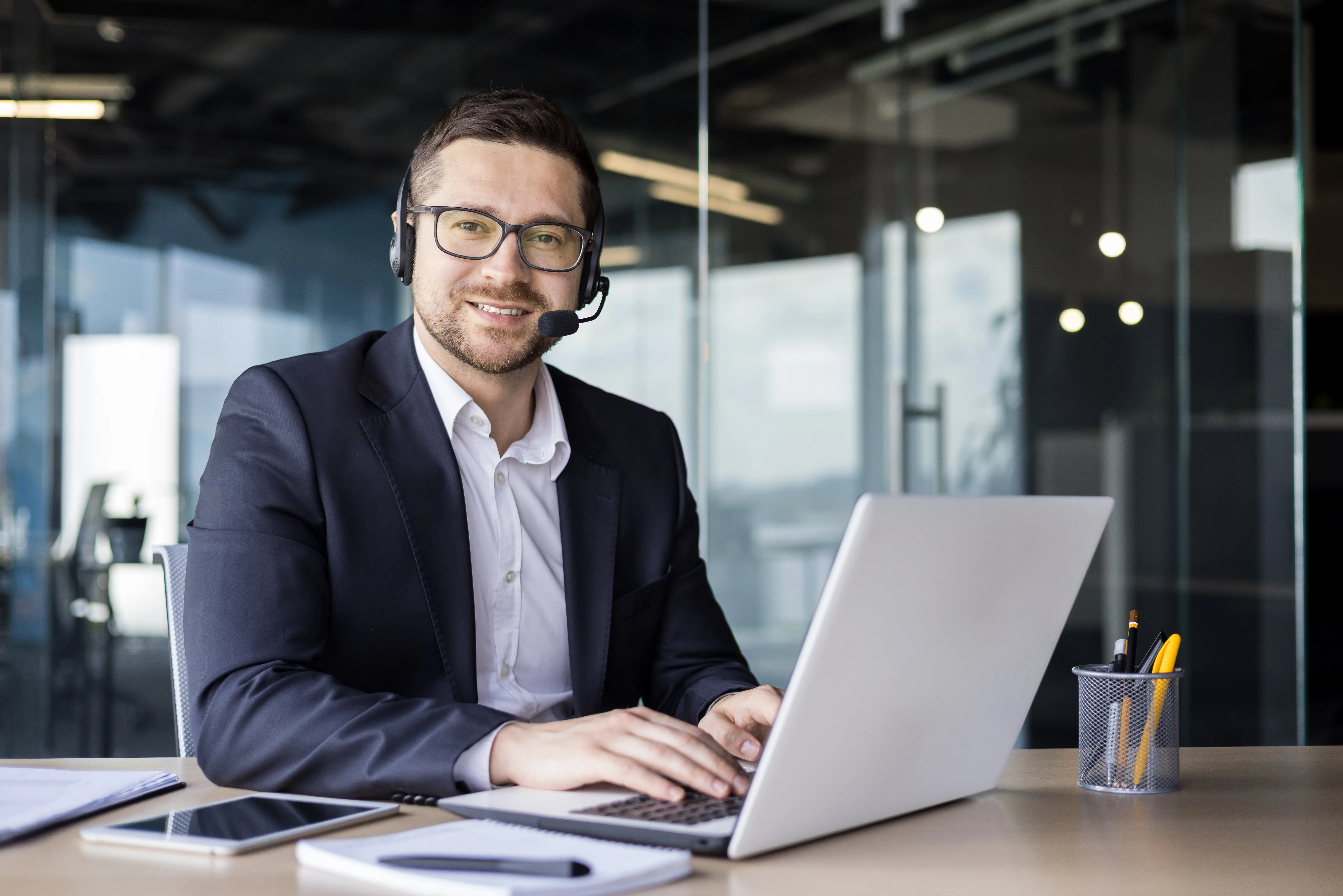 Freundlicher Mann im Anzug mit Headset am Computer 